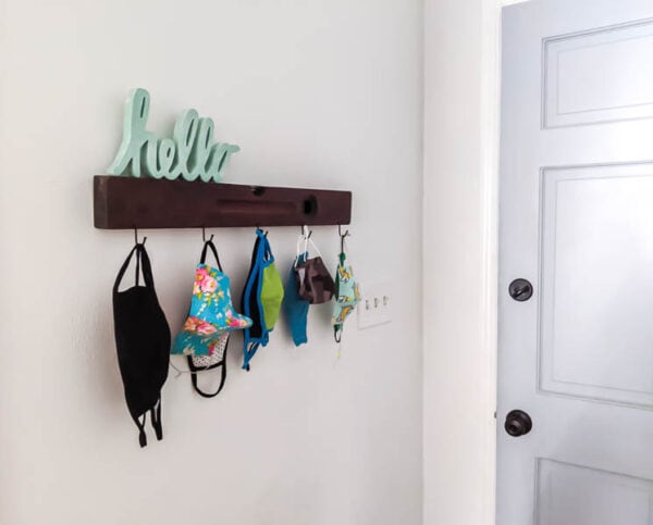 diy mask organizer made from an antique level and hooks, with different sized face masks hanging from the hooks