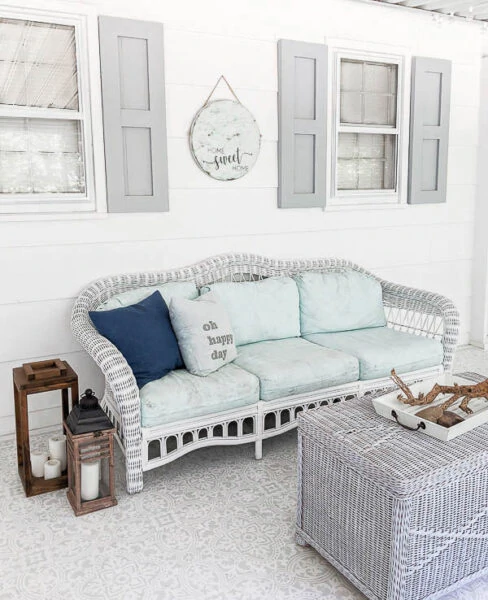 white wicker couch with painted cushions on white screened in porch with gray shutters