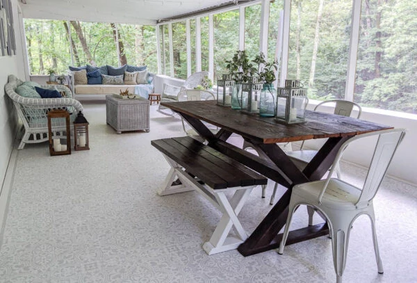 large screened in porch with stenciled floor, white wicker furniture, wooden dining table, and daybed