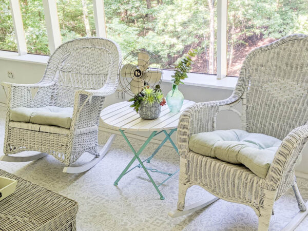 pair of white wicker rocking chairs on screened-in porch with blue and white table between them