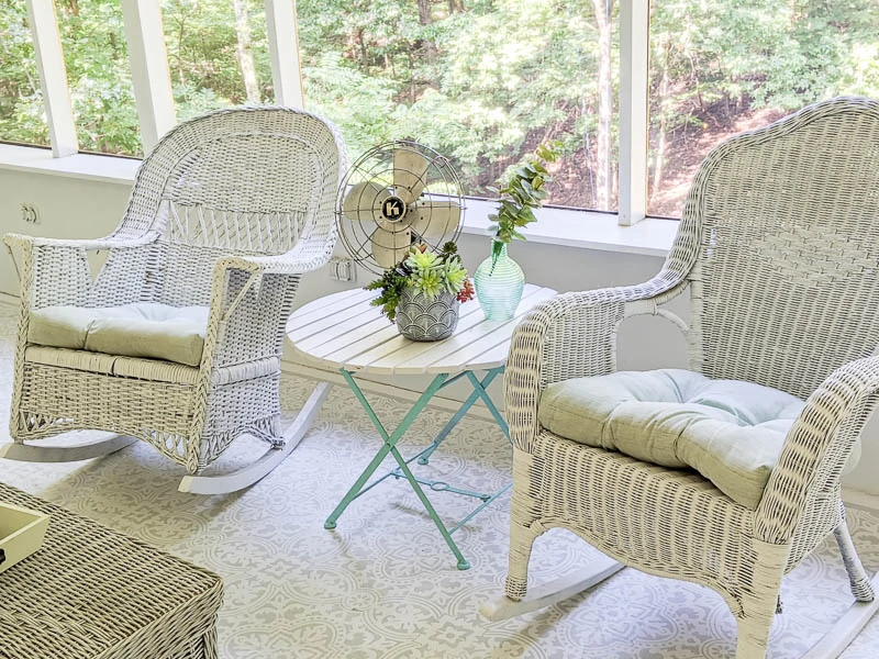 pair of white wicker rocking chairs on screened-in porch with blue and white table between them