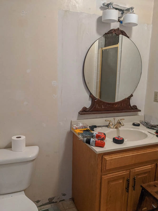 bathroom renovation in progress with patched walls waiting for paint, no baseboards, a vintage mirror, and tools everywhere.