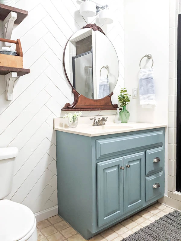 bathroom after $100 remodel with painted blue vanity, vintage mirror, and herringbone wood wall
