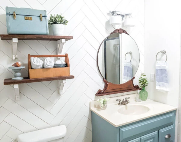 small bathroom with white herringbone shiplap wall, open shelves, and vintage wood mirror