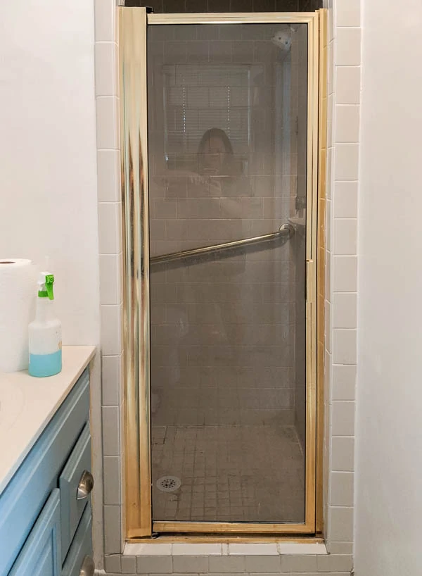 small shower with shiny gold shower door and beige tile.