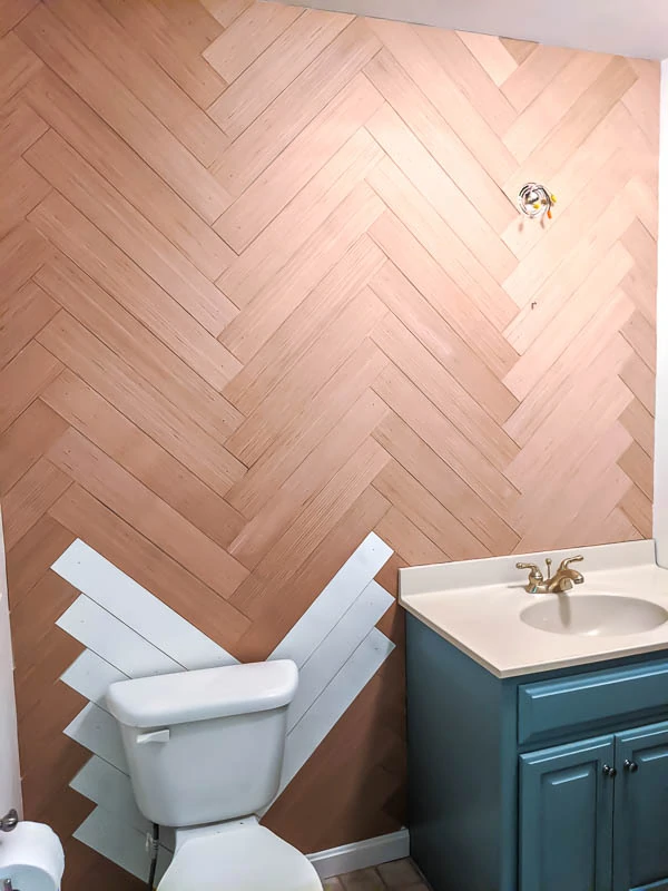 Completed herringbone wood wall with a few pieces of wood painted white behind the toilet.