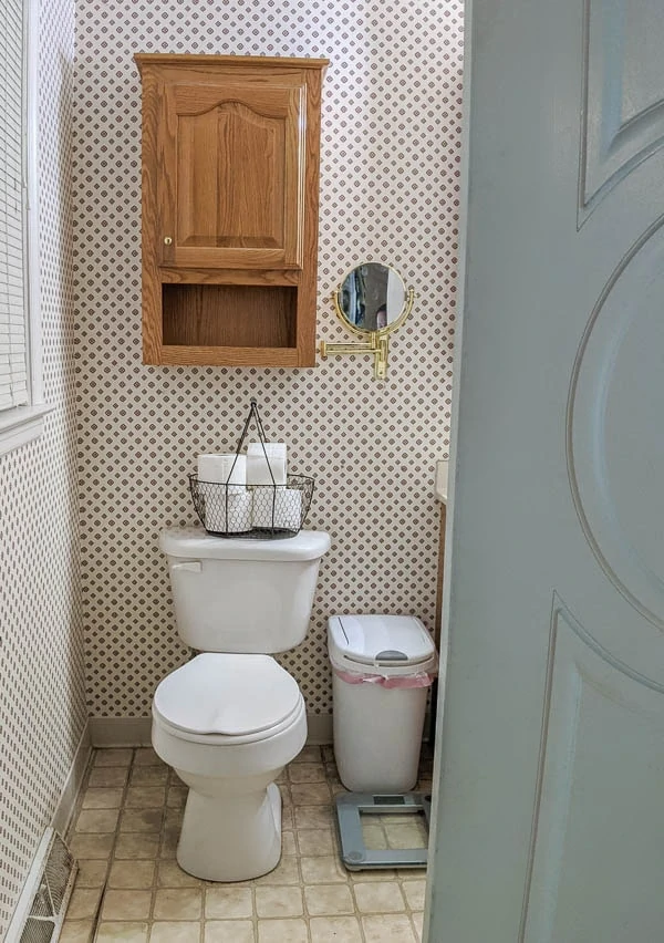 small bathroom with wallpaper with a diamond pattern, vinyl floors, and a big cabinet over the toilet.