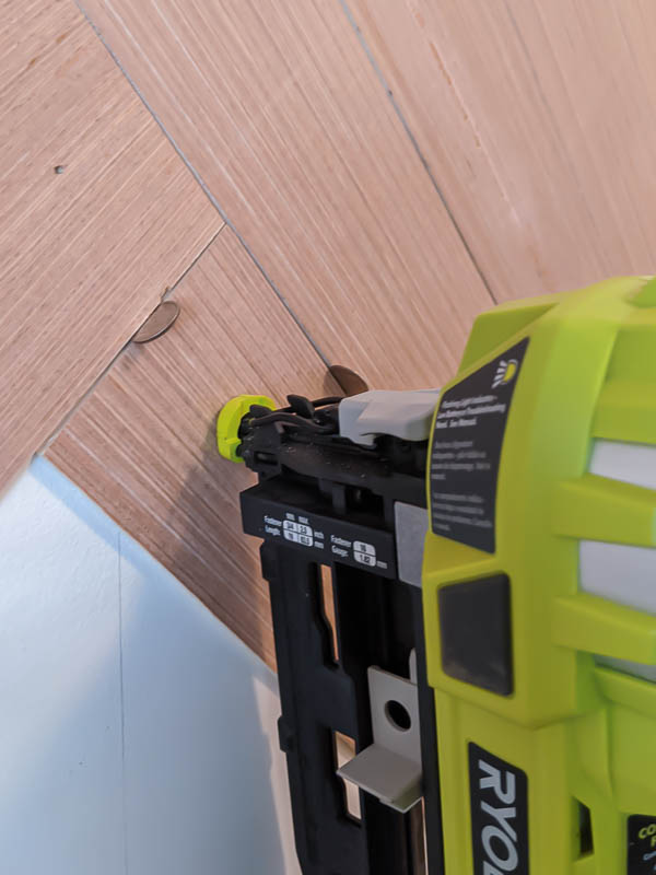 Nailing a board to the wall with a Ryobi nail gun, with dimes used to space the board evenly from the boards around it.