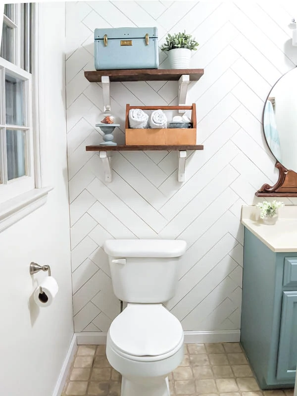 Reclaimed wood shelves with diy white wood shelf brackets against wood accent wall over toilet in small bathroom. 