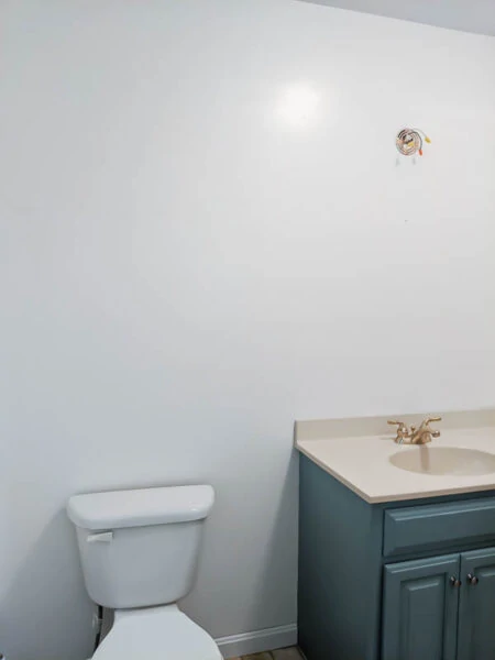 plain white bathroom wall with blue vanity and toilet.
