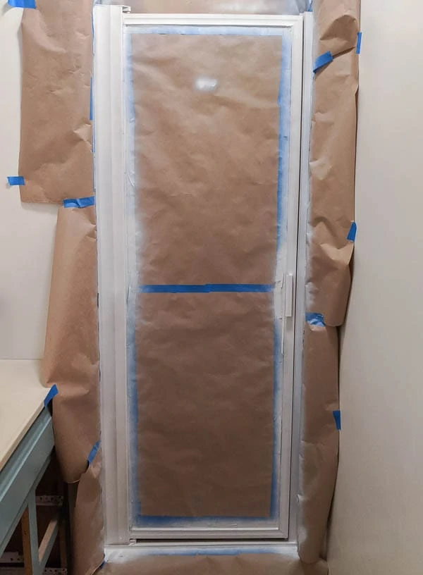 shower door frame surrounded by painters tape and primed with white spray primer