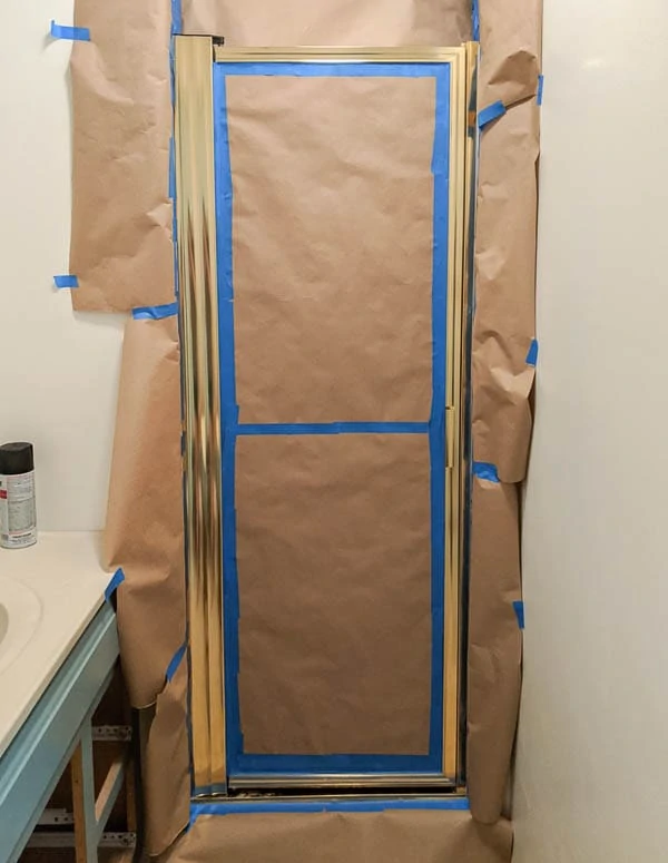 gold shower door surrounded by painter's tape and brown butcher paper to protect the walls from overspray