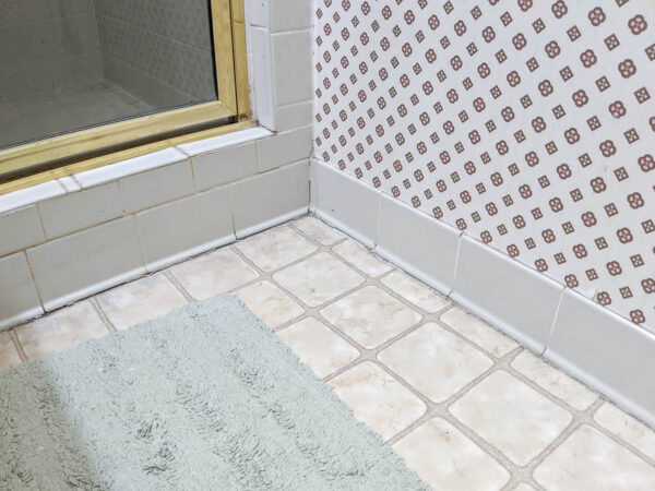 close up of vinyl floor with off white square pattern and border of beige tile around the bottom of the wall
