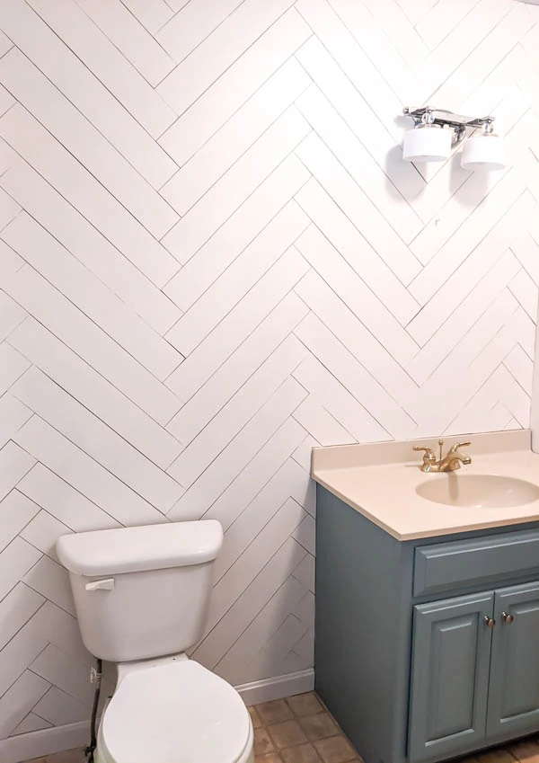 bathroom with white herringbone wood wall, blue vanity, and toilet.