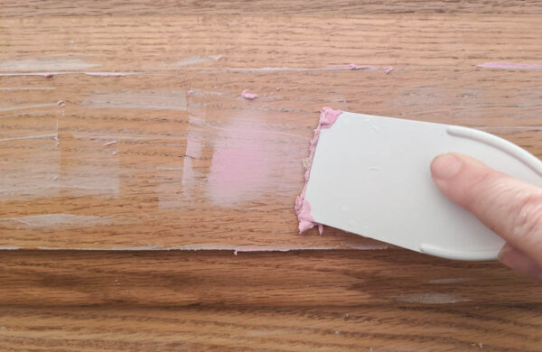using a putty knife to apply spackling to smooth wood grain in oak bathroom cabinets