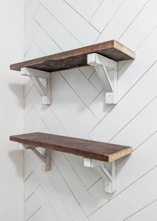 Reclaimed wood shelves with white diy wood brackets hanging on a white herringbone wood wall.