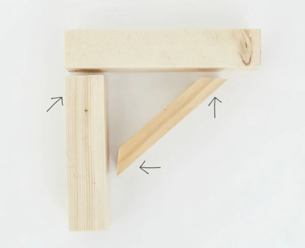 DIY wood shelf brackets with arrows pointing to the three spots where finishing nails are used to attach them.