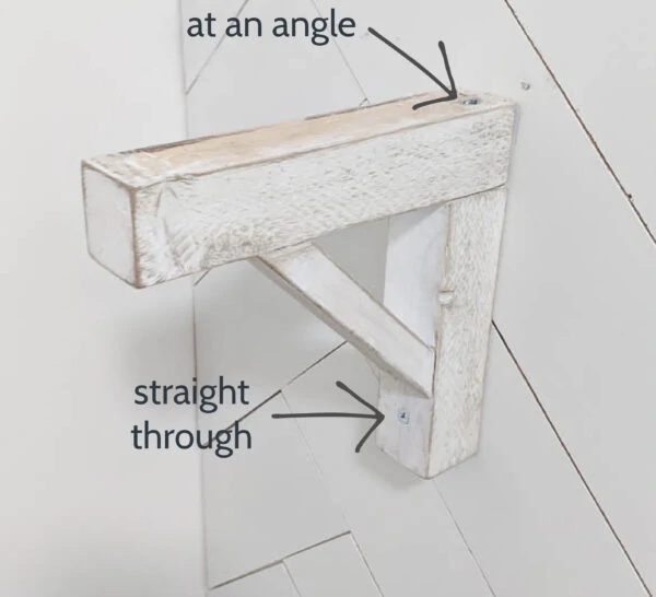 wood shelf bracket attached to the wall with two screws. Arrows point to the two places to attach the screws.