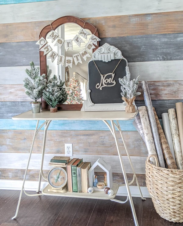 entryway with painted wood wall decorated for Christmas with vintage mirrors, glittery banners, and mini Christmas trees