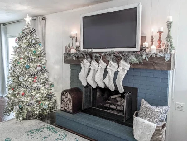 Fireplace with stockings, garland and lit candles next to flocked Christmas tree with white Christmas lights.