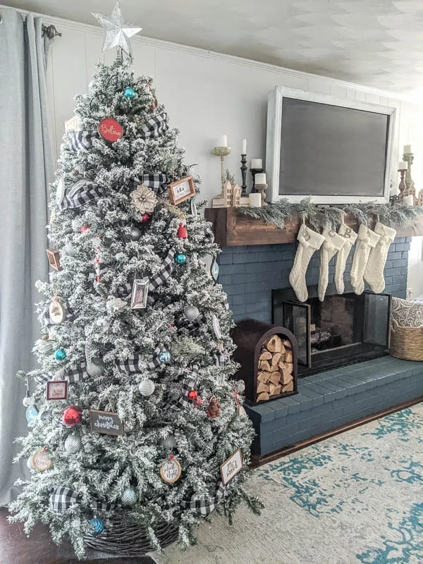 Flocked Christmas tree next to blue fireplace with white knit stockings and garland