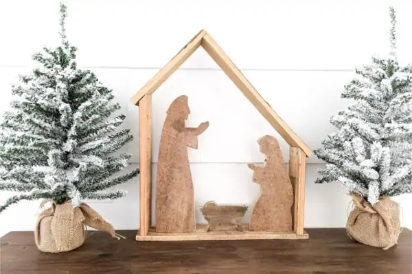 rustic wood nativity between two small Christmas trees.