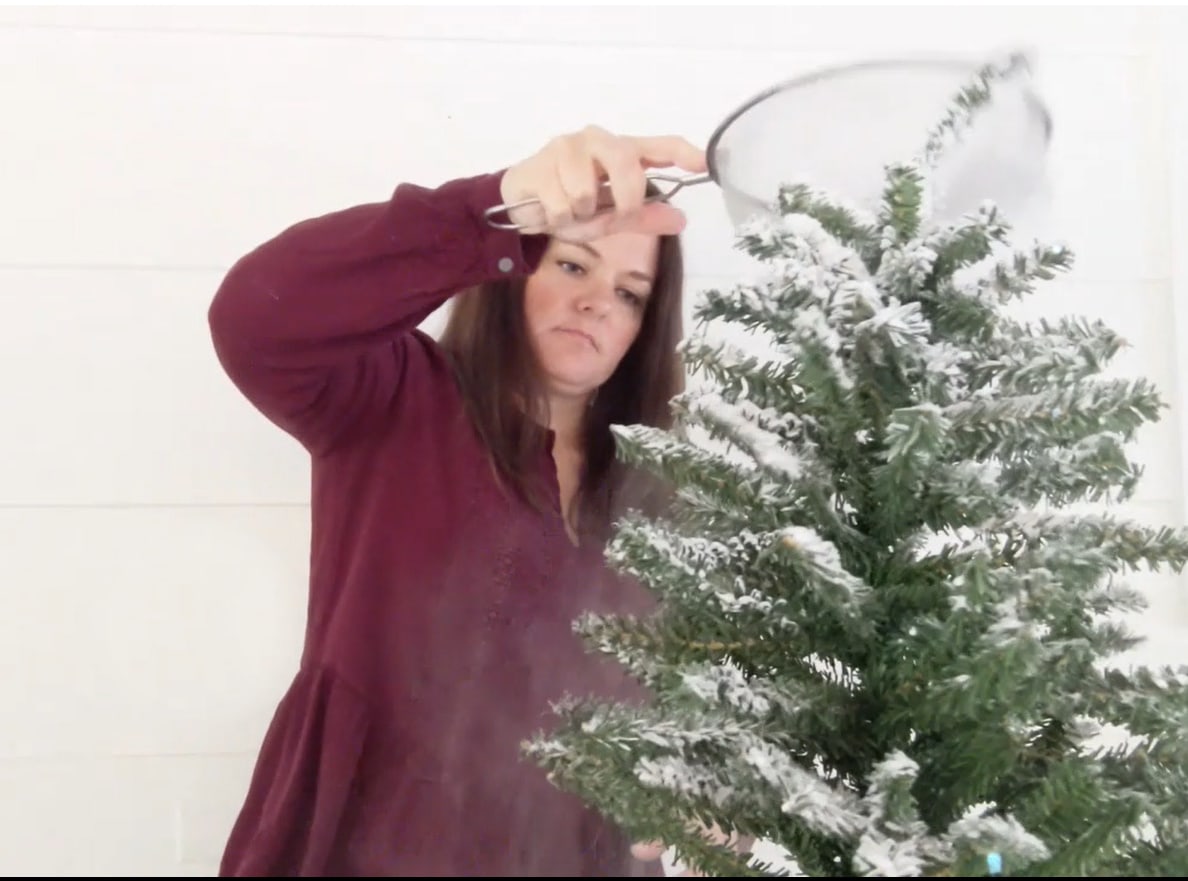 Flocking a small Christmas tree with a wire sifter and flocking powder.