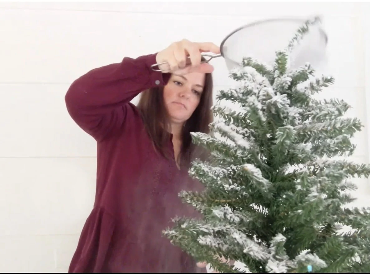 Flocking a small Christmas tree with a wire sifter and flocking powder.