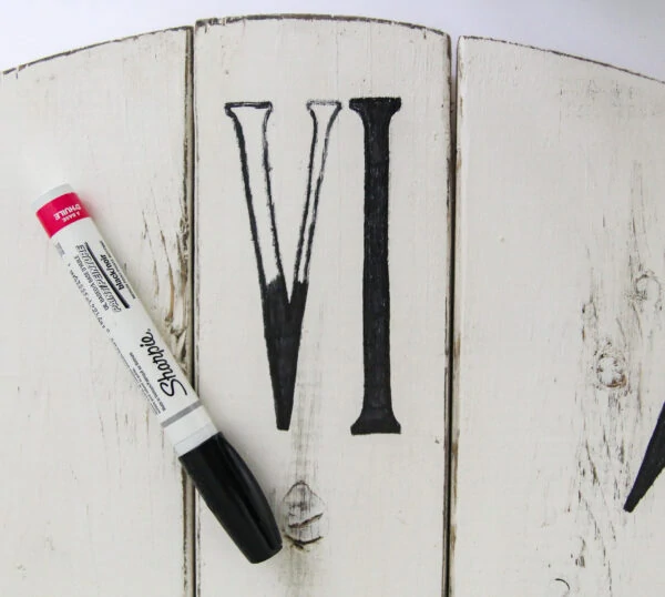 using a sharpie paint pen to fill in the numbers on a DIY oversized farmhouse clock.