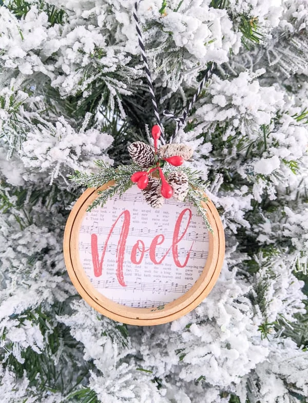 Noel embroidery hoop ornament hanging on flocked Christmas tree.