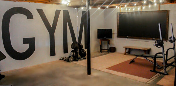 Unfinished basement home gym with gym mural wall and oversized chalkboard