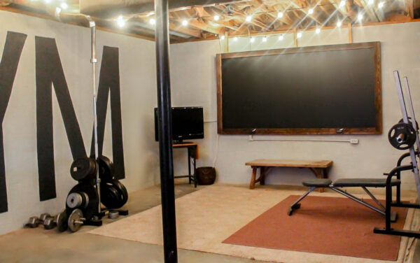 basement home gym makeover in unfinished basement with string lights and painted walls.