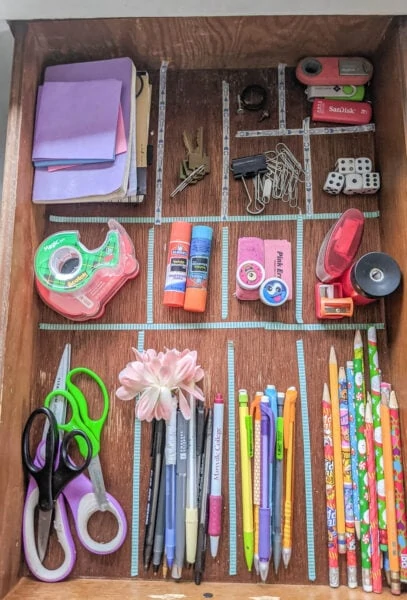 Everything in the junk drawer organized into piles with washi tape marking where the dividers will go.