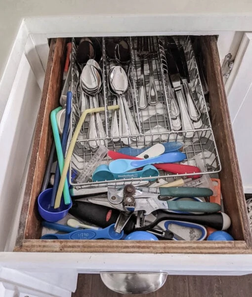 messy silverware drawer with a wire silverware organizer and other utensils crammed all around it.