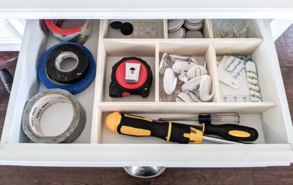 Junk drawer organized with diy drawer dividers with sections for command strips, duct tape, felt furniture pads, a tape measure, and screw drivers.