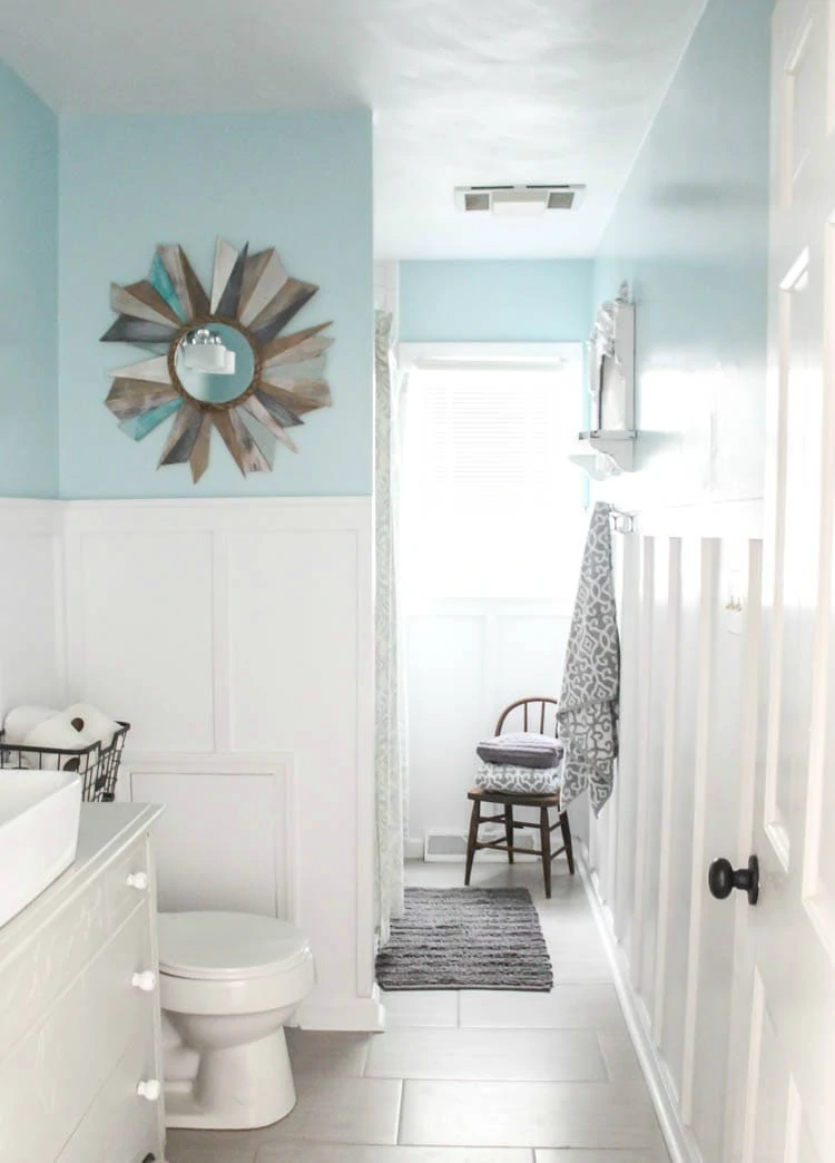 DIY bathroom renovation with board and batten, blue walls, tile floors, and an antique dresser vanity.