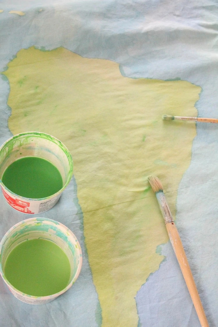painted outline of Africa on duvet cover with paint brush and cups of green paint.