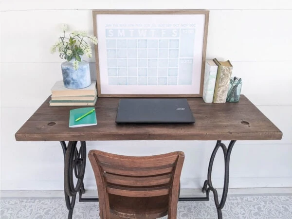 repurposed sewing machine table desk with laptop and pad of paper on top.