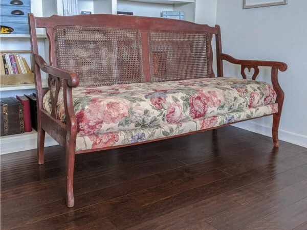 wooden settee with a cane back, a poofy floral seat, and heart cutouts on the arms.