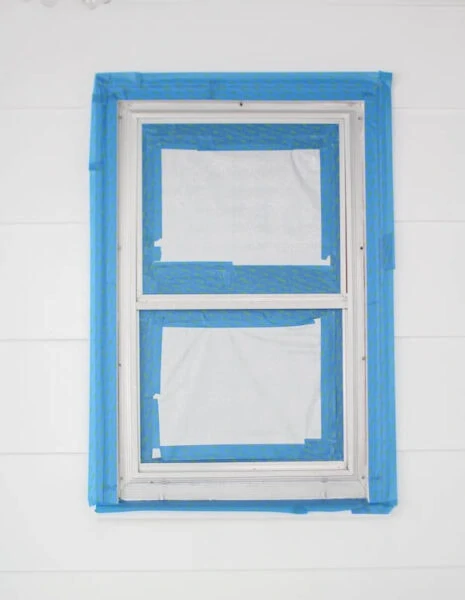 taping around aluminum windows to prepare them to be spray painted.