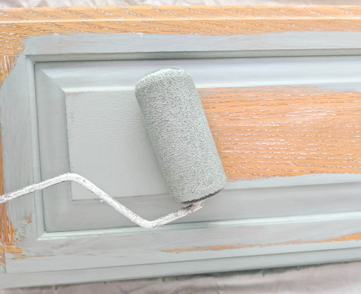painting a cabinet door with a flocked paint roller and blue paint.
