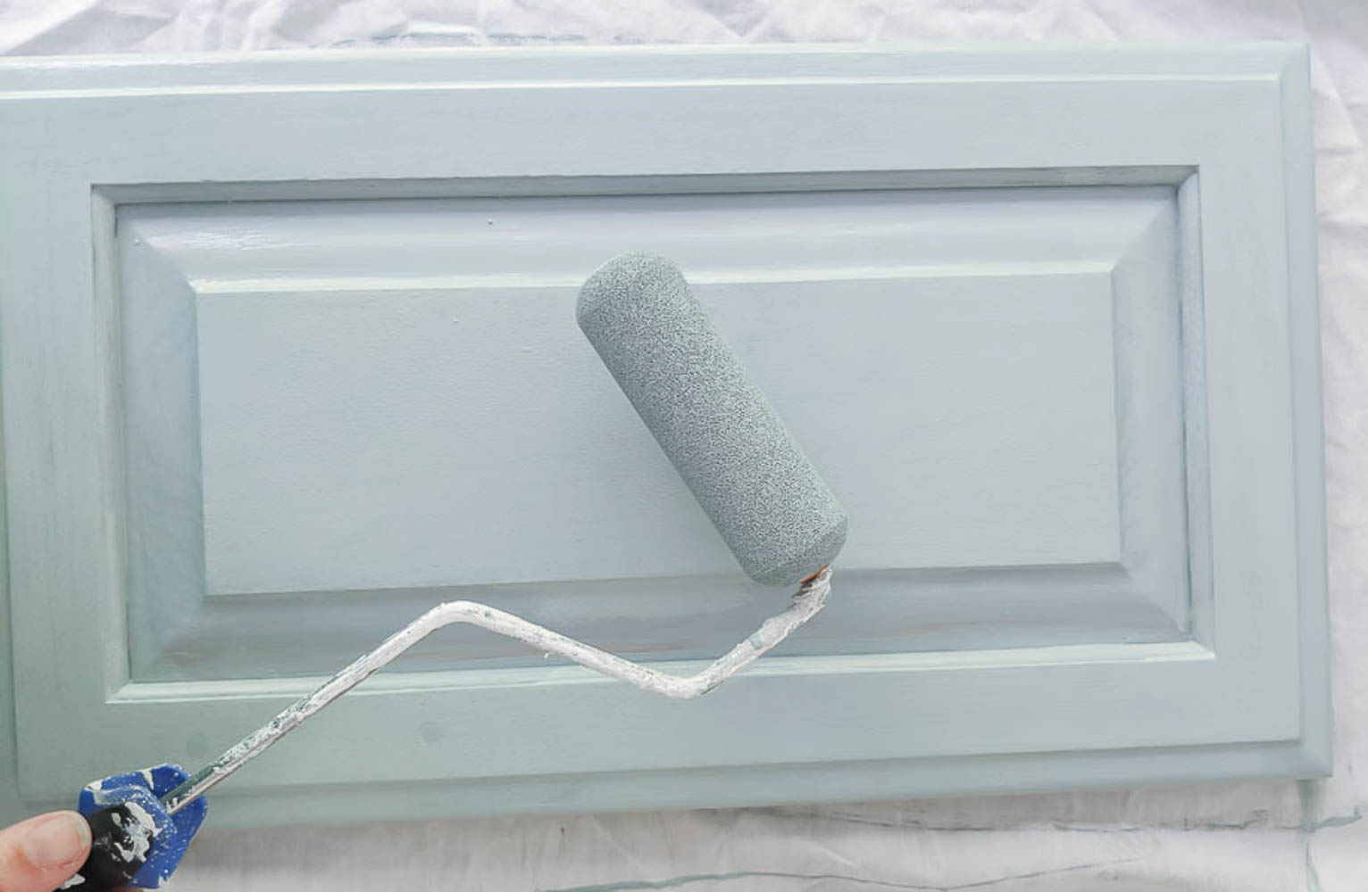 painting a cabinet door with a foam paint roller and blue paint.
