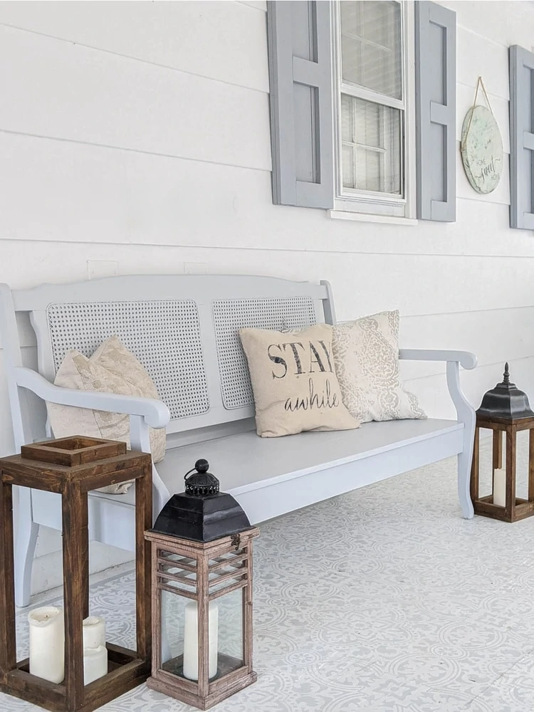 painted bench on porch with pillows and candle lanterns around it.