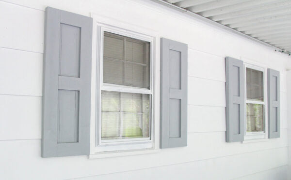 finished diy shutters painted gray and hanging next to two windows.