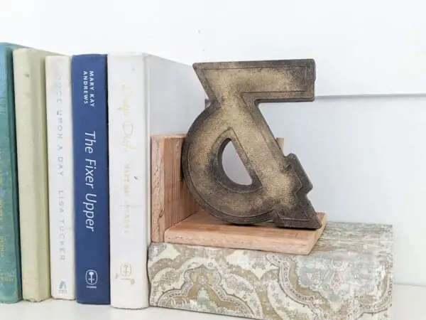 Vintage ampersand painted with a vintage brass paint finish, used as a bookend next to a stack of books.