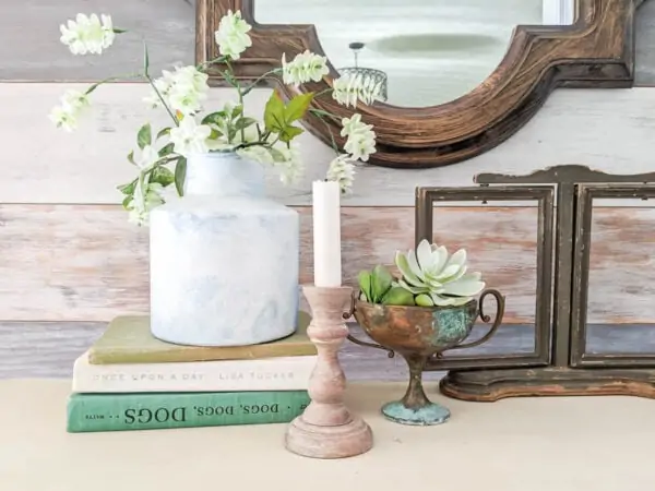 Candlestick painted with a weathered wood paint finish on a table next to old books and plants.