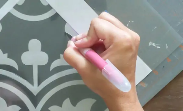Using a craft knife to cut a stencil design from plastic.