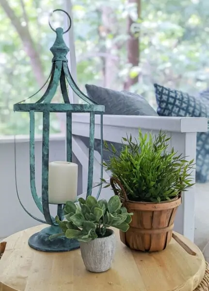 Thrifted candle lantern after it has been painted with a patina finish on a small table next to two plants.
