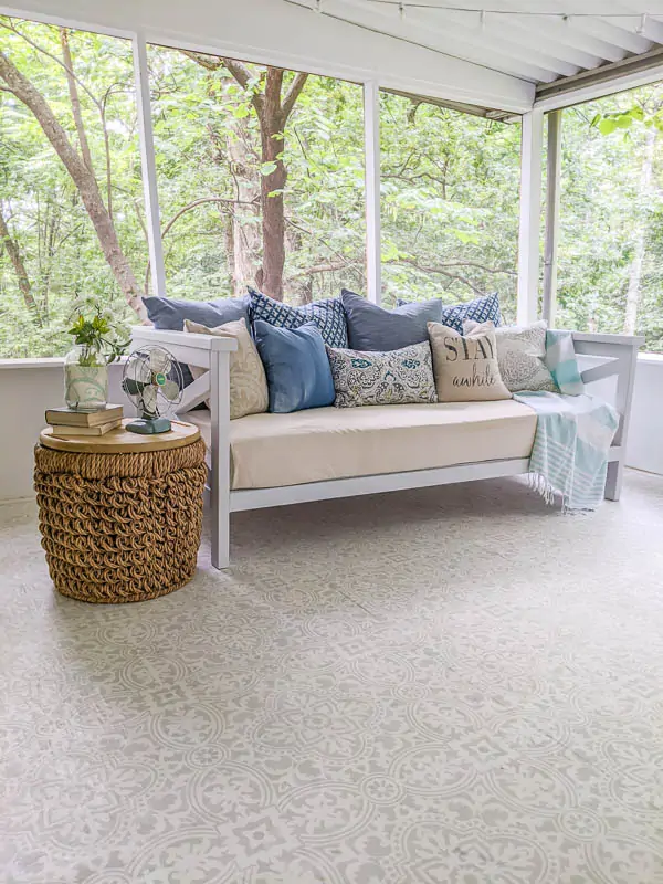 DIY daybed with piles of pillows and a basket table on a screened-in porch.