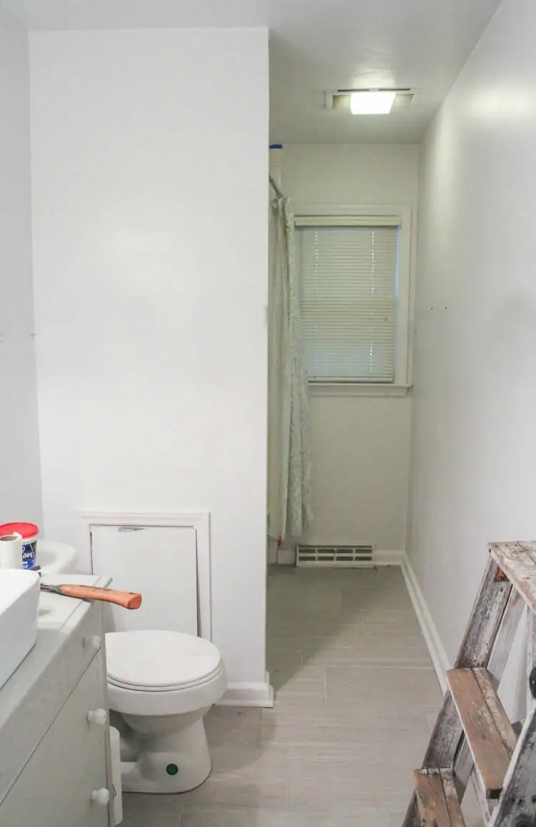 bathroom with light gray tile and plain white walls.